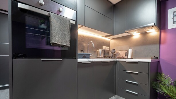 Uma cozinha moderna com armários escuros, forno embutido e torneira de aço inoxidável.
