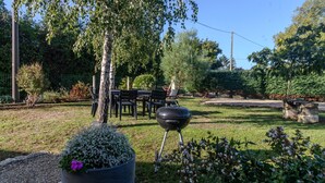A garden with a barbecue grill, outdoor seating, and a variety of plants. - Le logis chez bompain (Brizambourg)