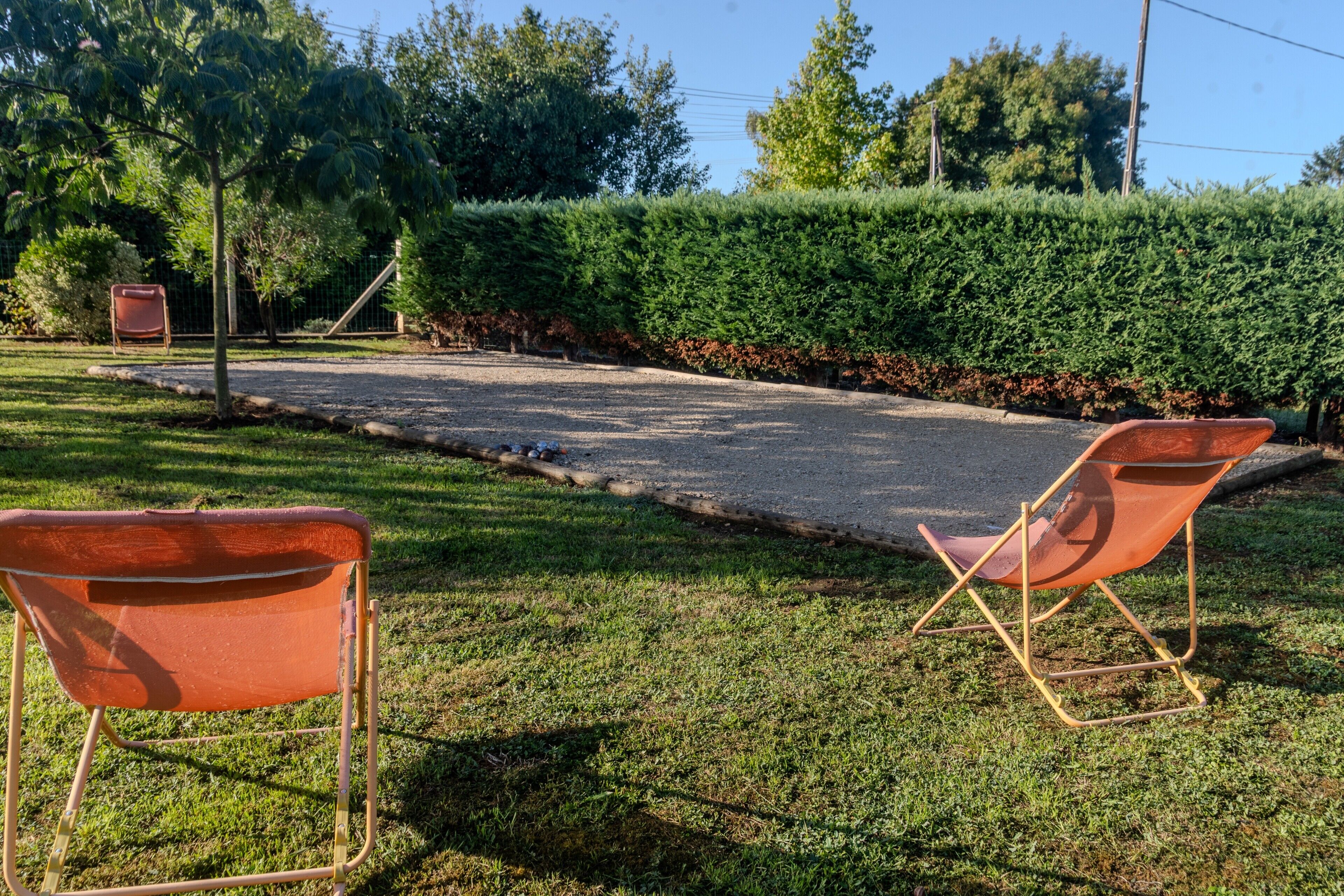 Uma trilha pavimentada, duas cadeiras dobráveis laranja e uma área gramada bem cuidada com um hedge.