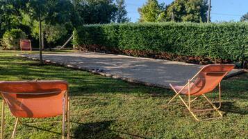 Uma trilha pavimentada, duas cadeiras dobráveis laranja e uma área gramada bem cuidada com um hedge.