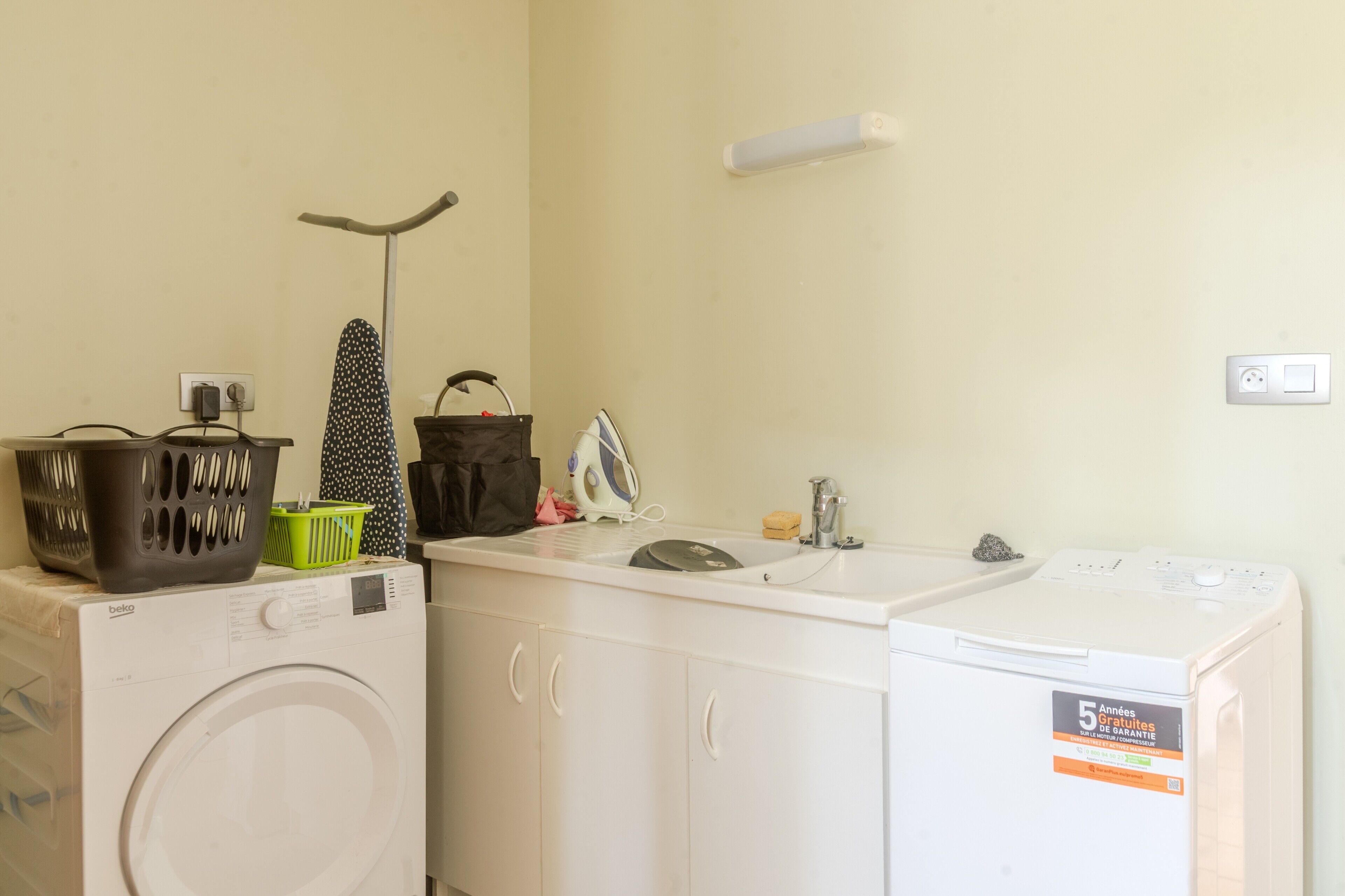 A laundry area with a washing machine, dryer, ironing board, and a sink.