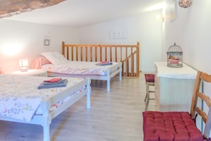 A bedroom with two beds, a wooden headboard, a small table with a birdcage, and a red chair. - Le logis chez bompain (Brizambourg)