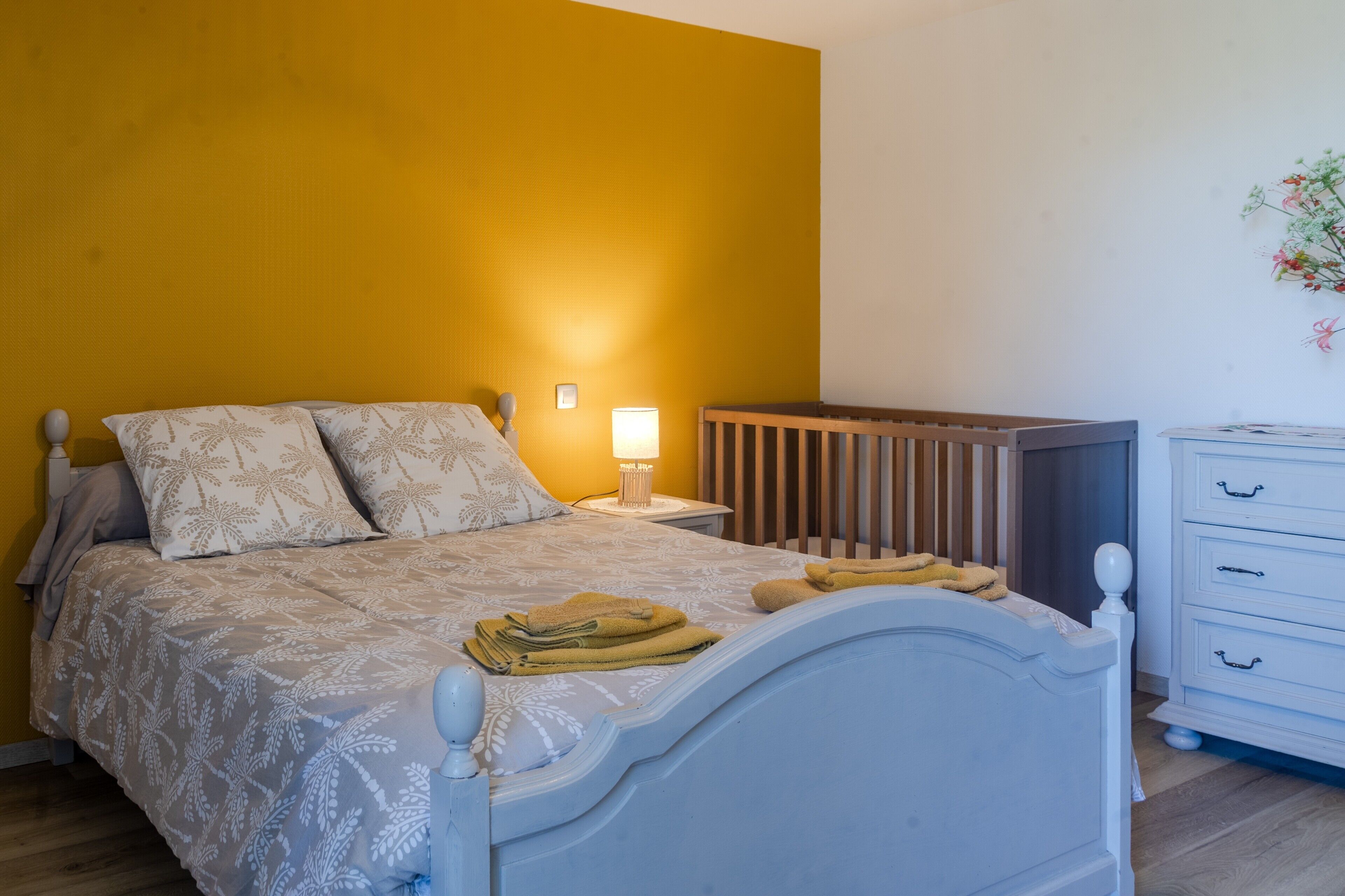 A bedroom with a bed, bedside table, lamp, and a dresser.