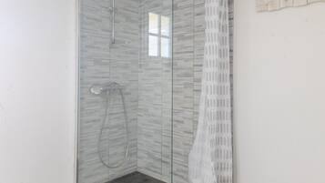 Eine gläserne Dusche mit gefliesten Wänden, einem kleinen Fenster und einem weißen Vorhang.