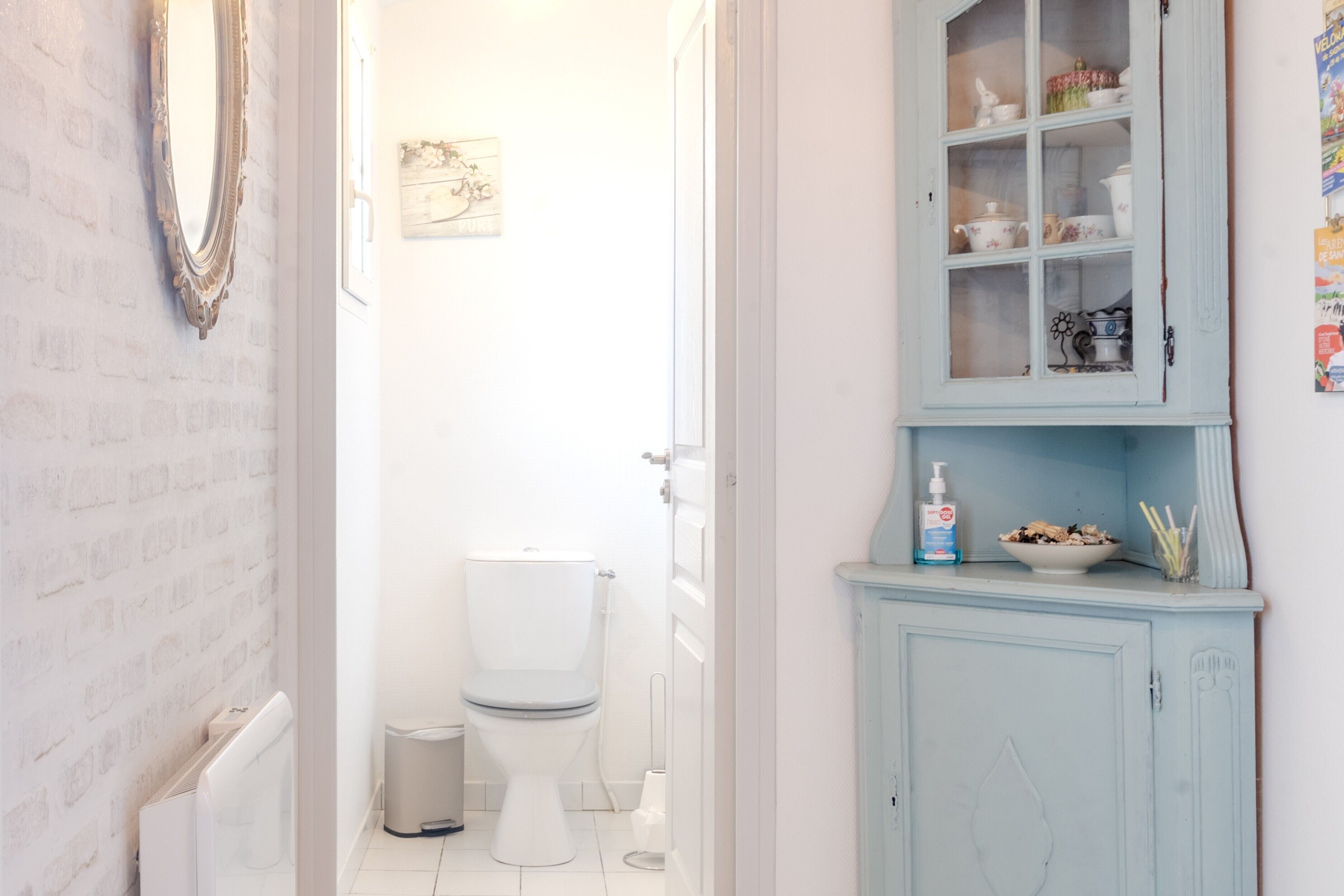 Un baño con un inodoro blanco, un armario azul con puertas de cristal y un radiador blanco.