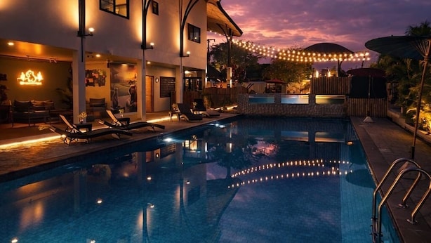 A swimming pool with lounge chairs, a covered area, and string lights against a twilight sky. - Capybara Zen Resort And Spa (Mae Pong)