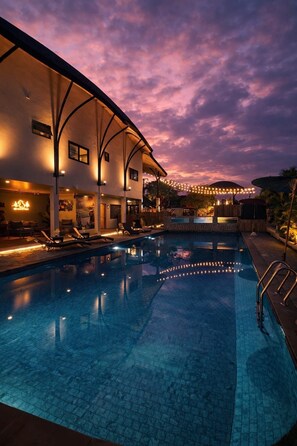 A swimming pool with lounge chairs, a covered area, and string lights against a twilight sky. - Capybara Zen Resort And Spa (Mae Pong)