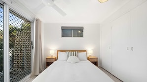 A bedroom with a large bed, two bedside tables with lamps, a window, and a wardrobe. - Beach Break: Firepit & Outdoor Entertaining (Caloundra Region)