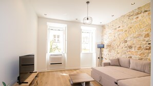 Una sala de estar moderna con una pared de piedra, un televisor de pantalla plana sobre un mueble de madera, un sofá beige y una pequeña mesa de centro de madera.