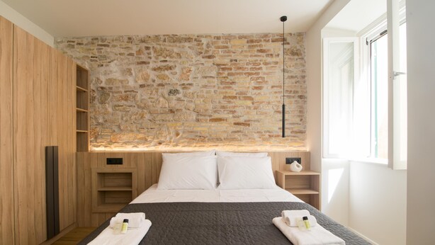 Un dormitorio con pared de piedra, cama con ropa blanca y armario de madera.