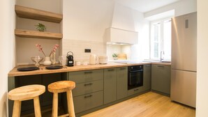 Una cocina moderna con encimeras de madera, dos taburetes, horno empotrado y refrigerador de acero inoxidable.