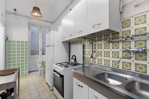 A compact kitchen with white cabinets, a gas stove, a sink, and patterned backsplash tiles. - Memories of yesteryear (Roma)