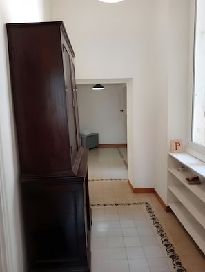 Un pasillo con un mueble de madera oscura, piso de baldosas con un borde decorativo, pared blanca y ventana con la letra 'P' en el alféizar.