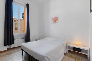 A bedroom with a single bed, a bedside table, a nightstand, a window with curtains, and a wall-mounted picture. - Memories of yesteryear (Roma)