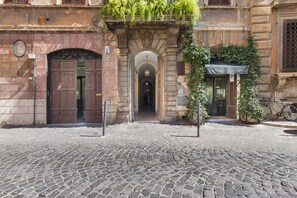Une rue pavée menant à un bâtiment doté d’une grande porte en bois et d’une entrée en arc de cercle.