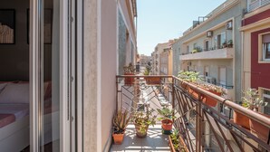 En balkon med plantekasser, en seng og udsigt til en gade med bygninger.