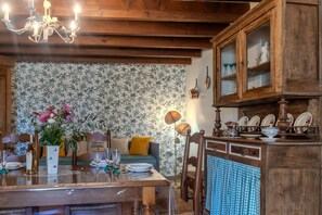 Ein Essbereich mit einem Holztisch, Stühlen, einer Chandelüster, einer Couch und einem Schrank mit Glastüren.