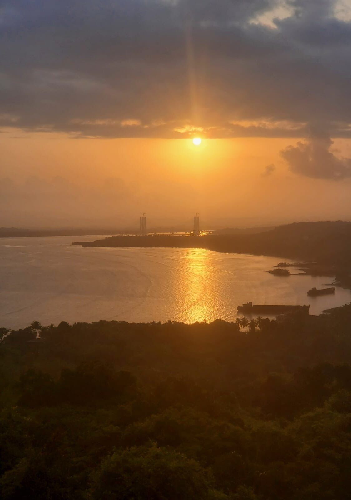 Ein Sonnenuntergang über einem Gewässer mit Gebäuden in der Ferne und einer hügeligen Landschaft.