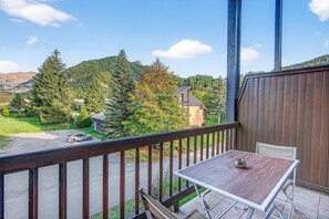 A balcony with a table and chairs, overlooking a mountainous landscape with trees and a road.
