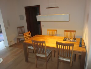 Un coin repas avec une table en bois et quatre chaises, un luminaire suspendu et une porte visible au fond.