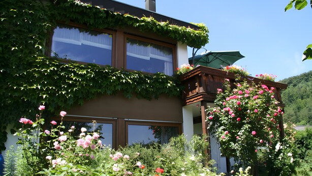 Een huis met een tuin, een houten balkon en een raam met gordijn.