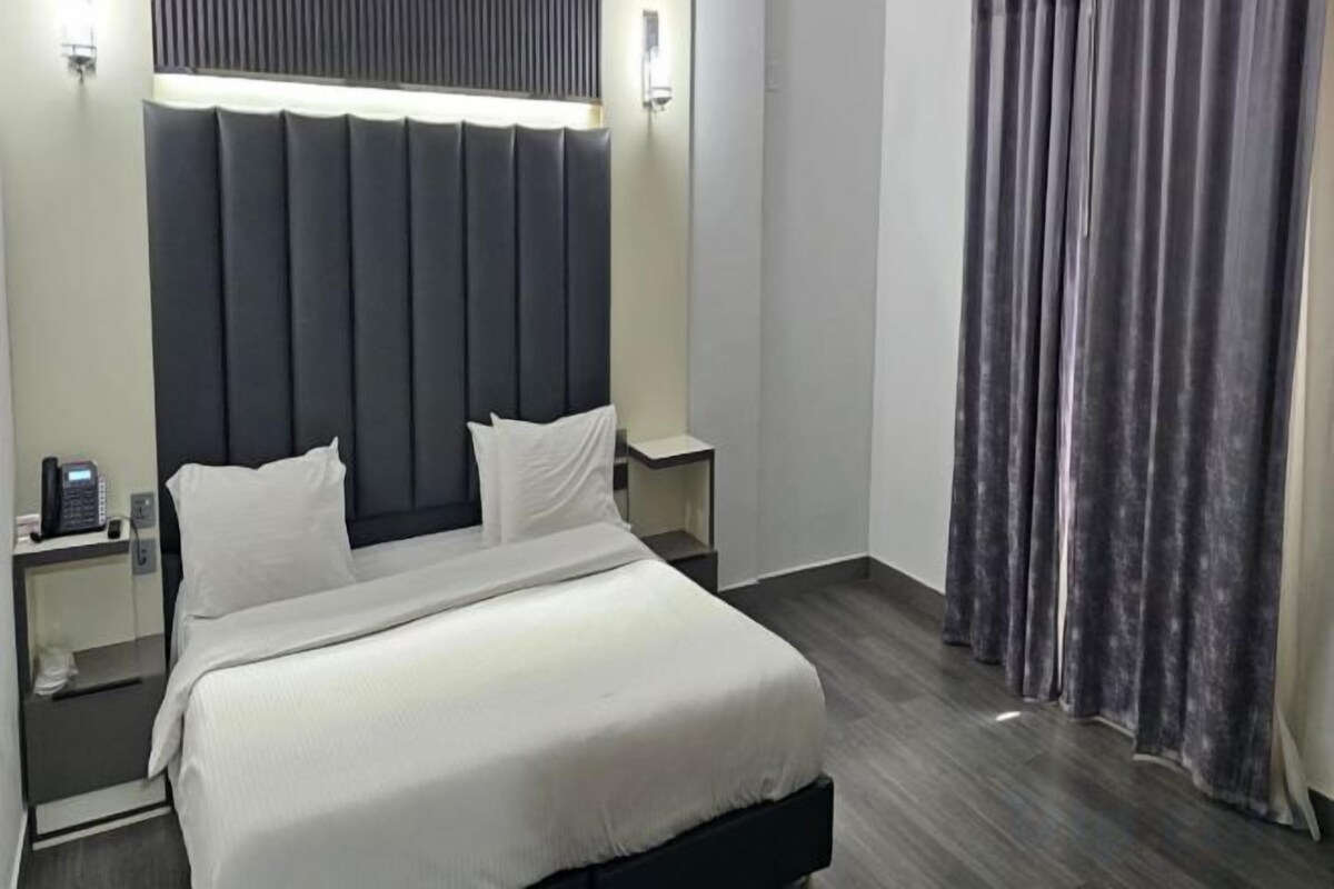 A hotel room with a large bed, bedside tables, a telephone, and a curtain.