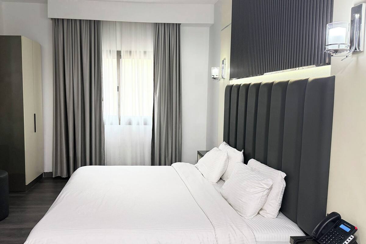 A hotel room with a large bed, a bedside telephone, a wardrobe, and a mirror.