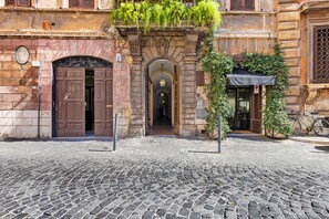 Una calle adoquinada con un edificio que tiene una puerta de madera grande, una entrada en arco y una pequeña tienda con un letrero.