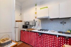 Une cuisine compacte équipée d’un four à micro-ondes, d’une cuisinière et d’un évier. On y trouve des étagères fixées au mur et un panier accroché à la porte.