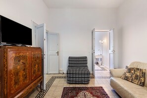 Un salon comprenant un téléviseur, un pouf à motifs, un canapé et un meuble.