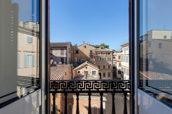 Vista desde una ventana con balaustrada, que da a una calle con edificios históricos y un cielo despejado.