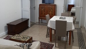 Una sala de estar con un sofá, una mesa de comedor con sillas, un televisor sobre un mueble bajo y una alfombra estampada.