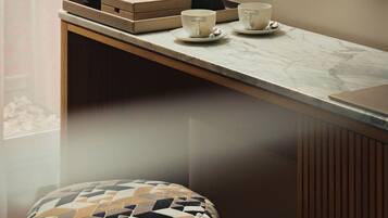 A modern room with a wooden console table, a patterned ottoman, and a large window with sheer curtains.