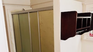 Une salle de bain avec un espace douche, un carrelage blanc au sol et un mur blanc avec une étagère.