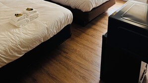 Une chambre d’hôtel avec deux lits, un plancher en bois, une fenêtre avec des stores et une petite table.