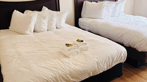 Deux lits simples avec des têtes de lit sombres et du linge de lit blanc, un plancher en bois et une petite serviette sur le lit.