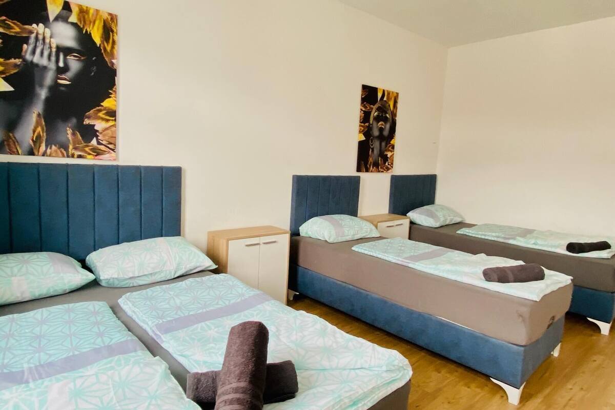 A hotel room with three beds, each with a headboard, a small bedside table, and a pillow.