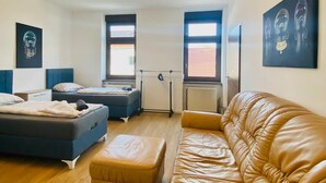 A modern, well-lit room with a large leather sofa, two single beds, and artwork on the walls. - Spacious 4BR for 15 & 15 Min to Danube (Vienna)