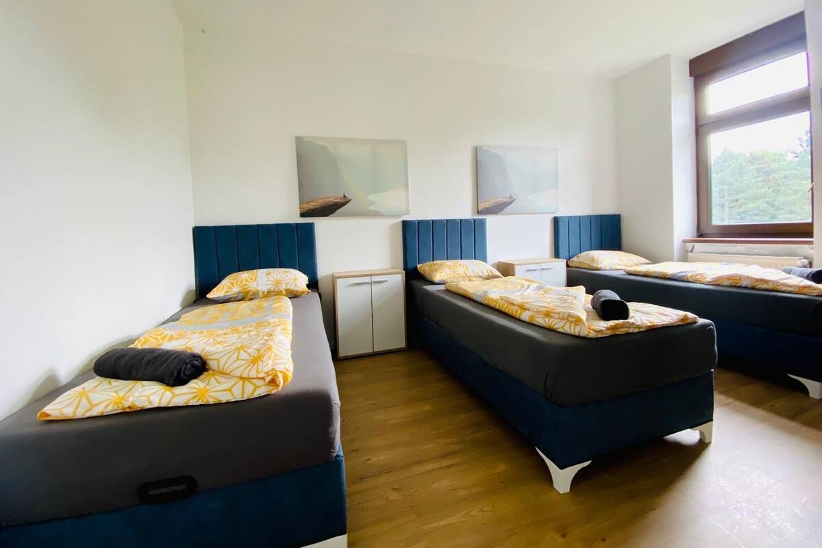 A room with three single beds, each with a headboard and a pillow. There is a small cabinet between the beds.