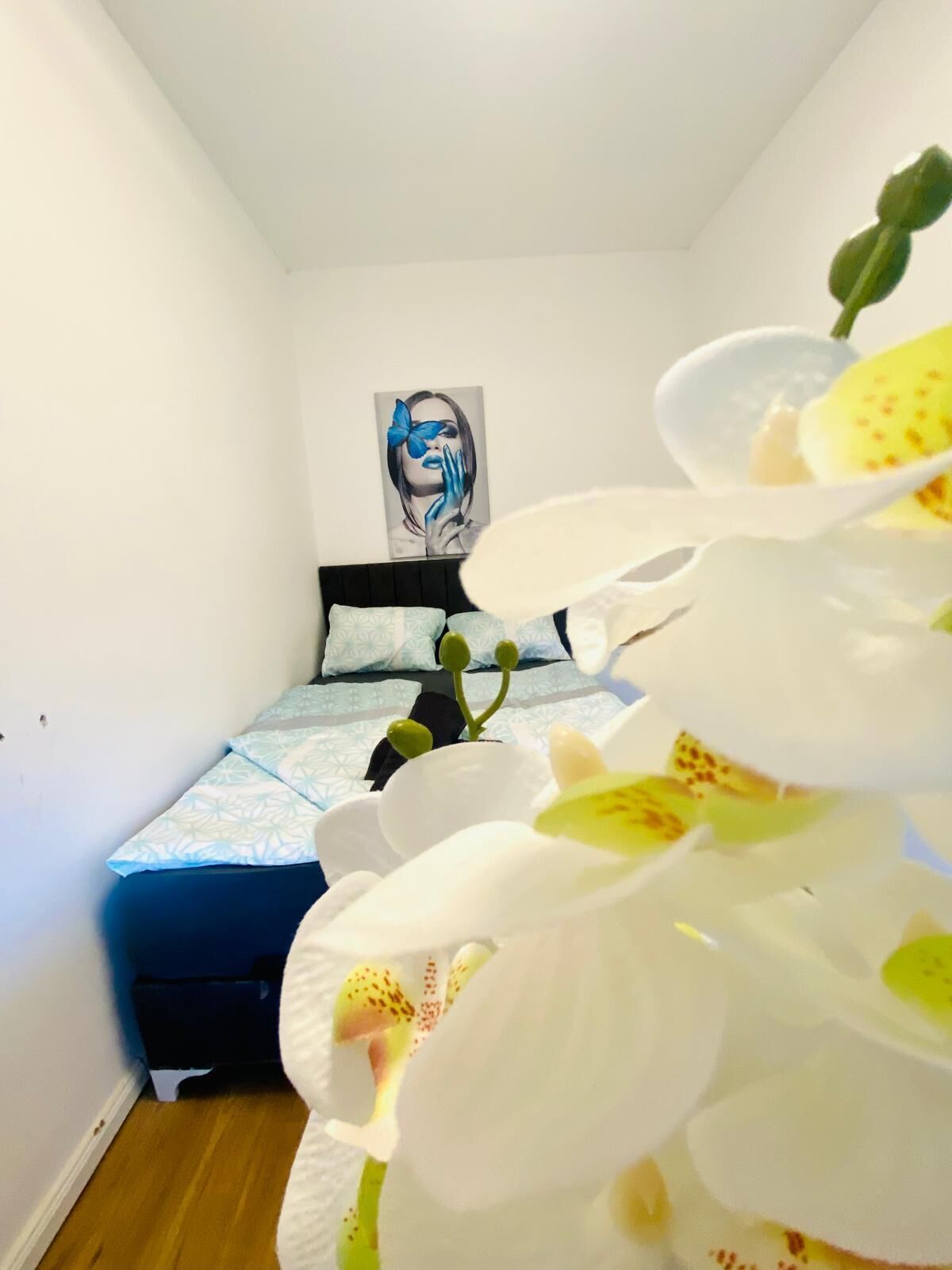 A bedroom with a bed, a painting on the wall, and a large orchid plant.