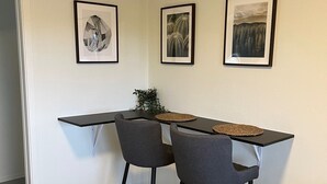 Ein kleiner Essbereich mit einem schwarzen Tisch und zwei grauen Stühlen, gerahmten Bildern an der Wand und einer Pflanze auf dem Tisch.