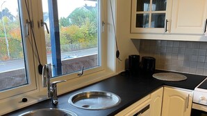 Eine Küche mit zwei Edelstahl-Spülen, einer schwarzen Arbeitsplatte, weißen Schränken, einem Fenster mit Blick auf Bäume und einer gefliesten Spritzschutzwand.