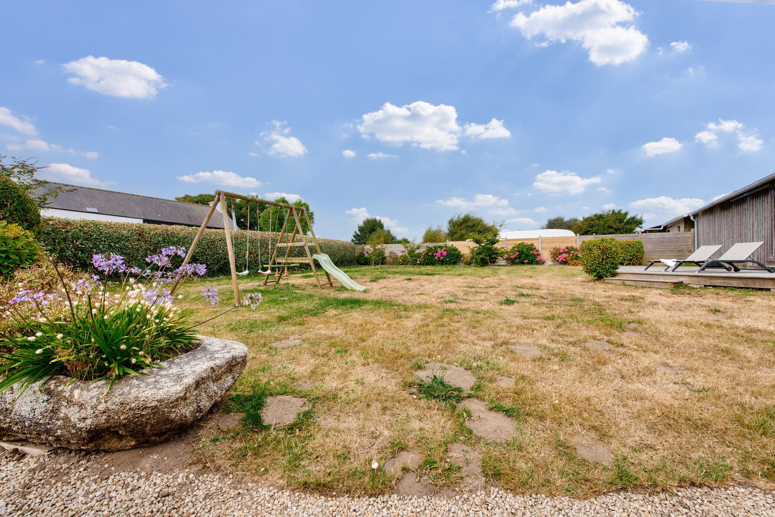 Un jardin avec une balançoire, un toboggan et des fleurs violettes.