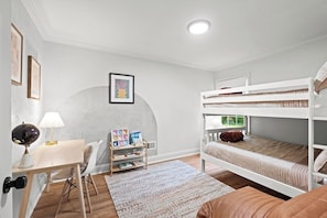 Une chambre avec des lits superposés, un bureau avec une lampe, une chaise, une bibliothèque et un tapis.