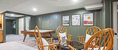 Ein Zimmer mit Billardtisch, Korbstühlen und gerahmten Bildern an der Wand.