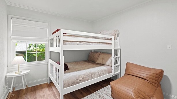 A bunk bed room with a window, a small table with a lamp, and a brown chair.