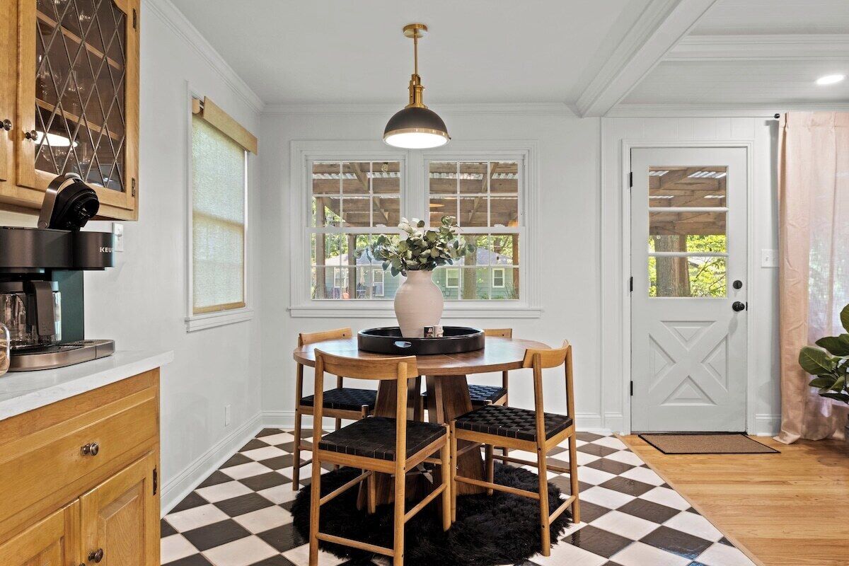 Uma área de refeições com mesa redonda, cadeiras, um vaso com flores e uma luminária pendente.