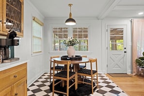 Un coin repas avec une table ronde, des chaises, un vase de fleurs et une suspension.