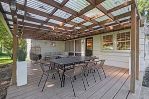 A covered patio with a wooden table and chairs, a cushioned bench, and a potted plant. - The Glenwood - A Cozy Ranch in Mission, KS (Mission)