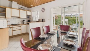 A modern kitchen with wooden cabinets and a dining area with a glass table and red chairs. - Garden and veranda - House 4 adults 2 children (Saint-Hilaire-de-Riez)